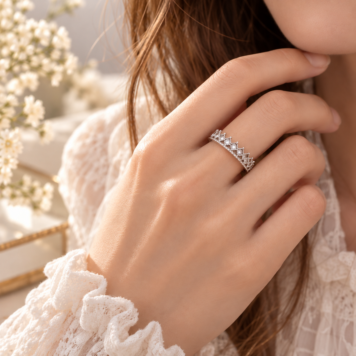 Bague couronne argentée portée au doigt, motif diadème et pierres transparentes