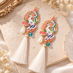 Boucles d’oreilles phénix et fleurs roses avec pompons blancs, présentées à plat