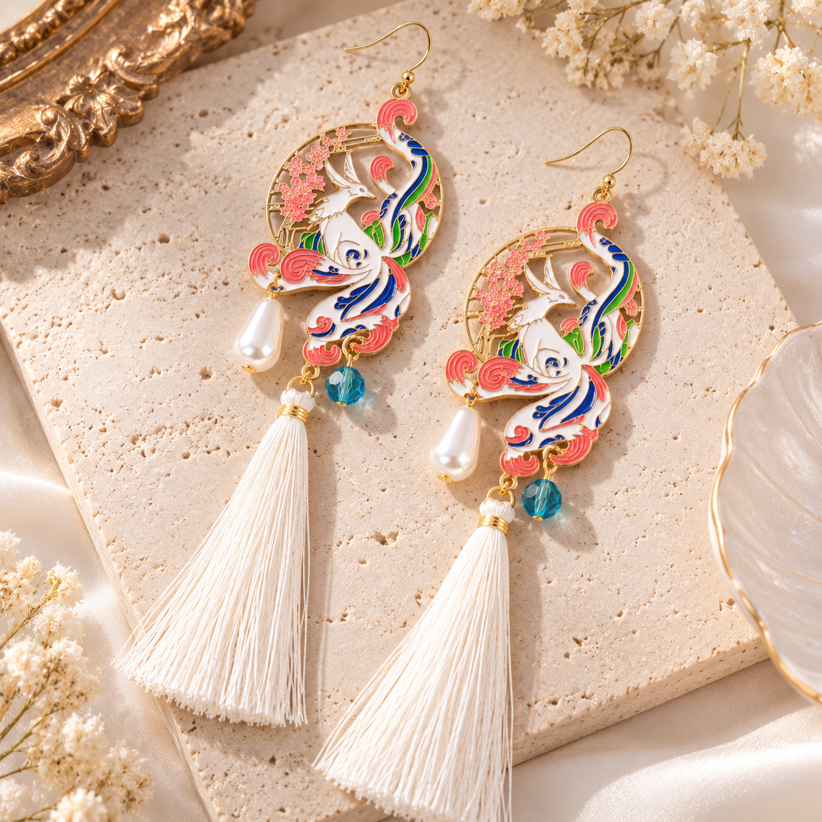 Boucles d’oreilles phénix et fleurs roses avec pompons blancs, présentées à plat