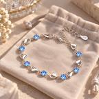 Bracelet argenté à cœurs et pierres bleues présenté sur une pochette en velours