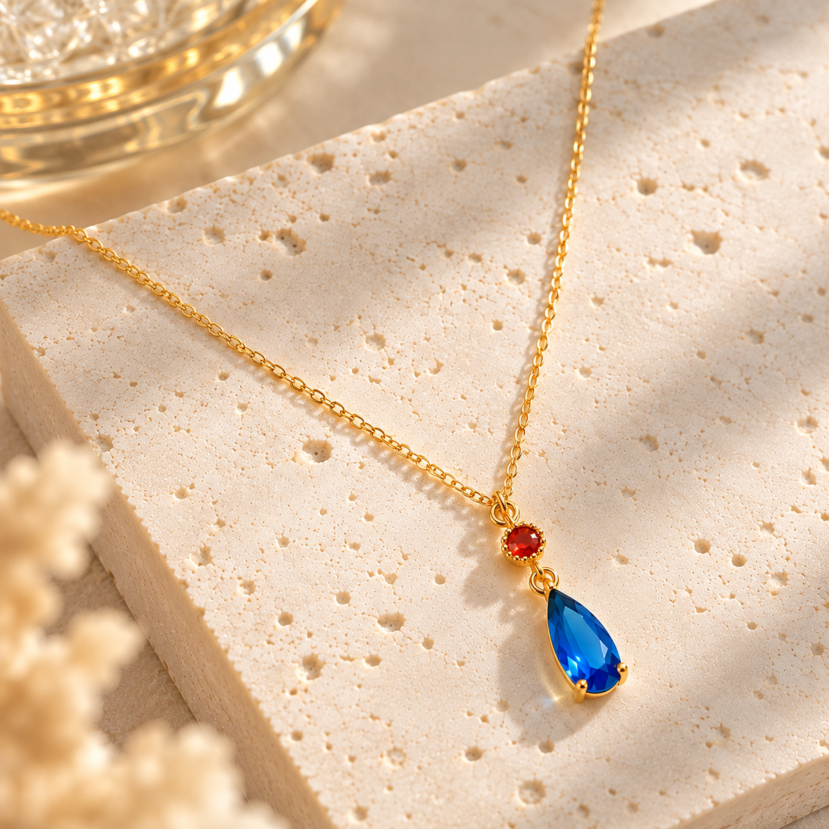 Collier doré avec pendentif goutte bleue et détail rouge