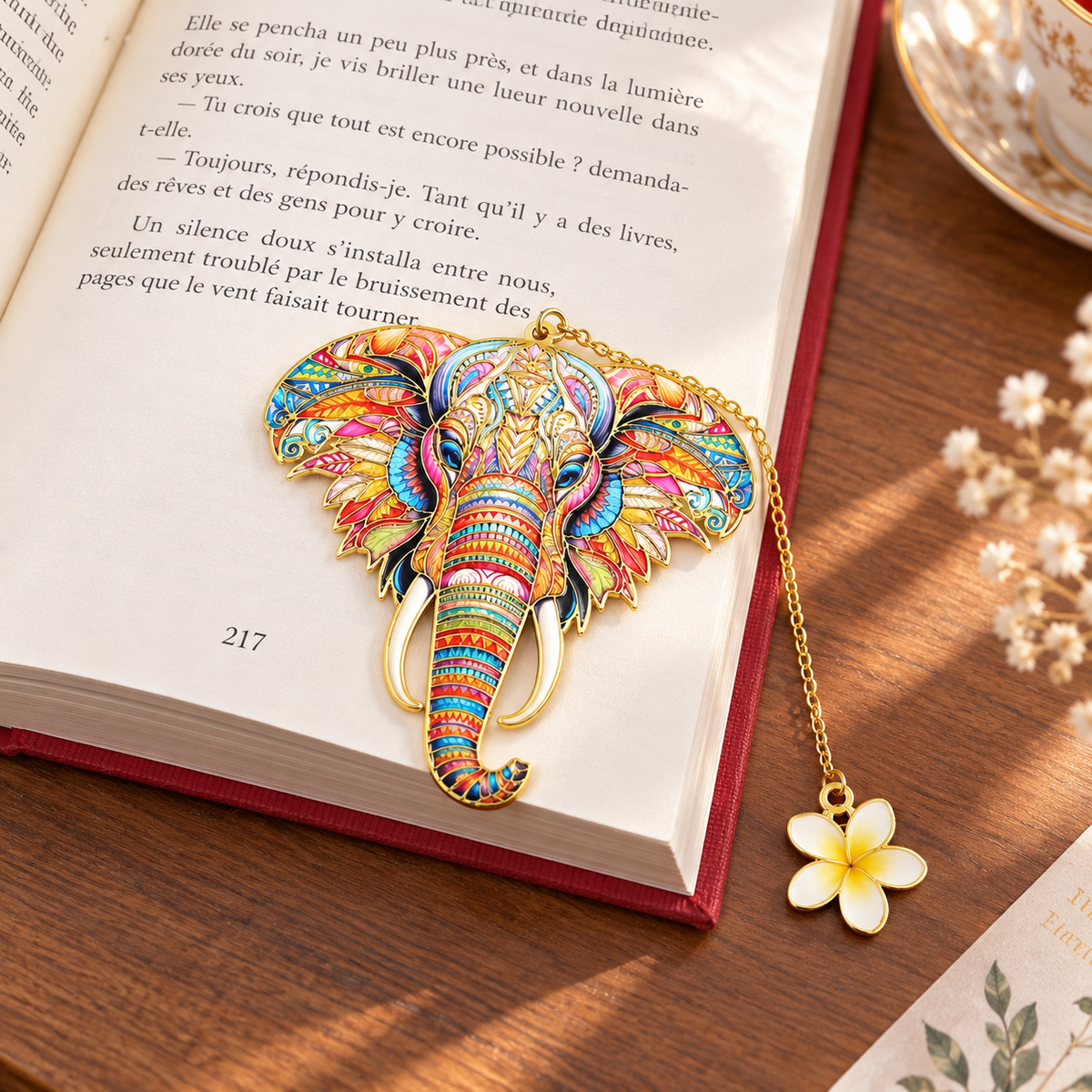 Marque-page éléphant multicolore posé sur un livre ouvert avec breloque fleur